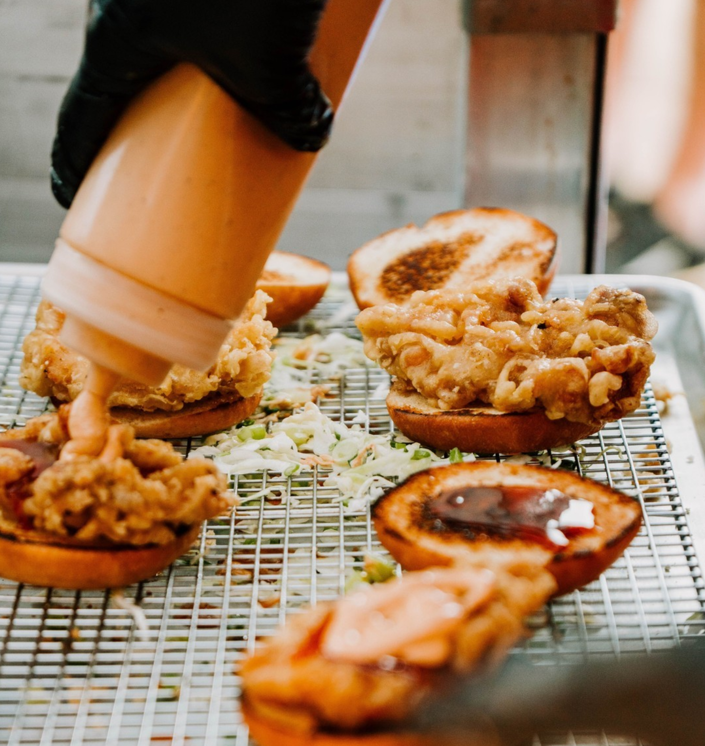 An image of sauce being squeezed onto a Mamahuhu Chicken Sandwich